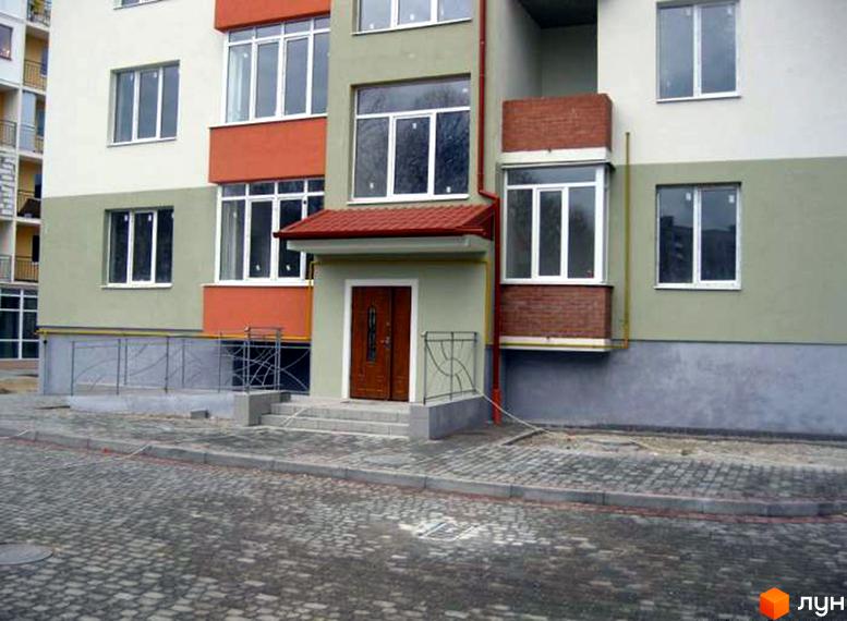 Житловий будинок на Караджича, 29а, 29в, 29г: бежево-зелений фасад, білі вікна, помаранчеві акценти. Вхід з коричневими дверима та бруківка.