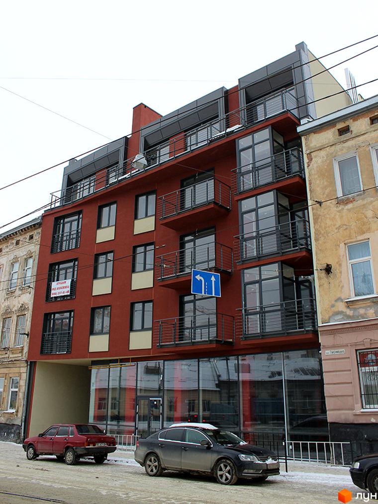 Новобудова на вулиці Гайдамацькій, 12а, з червоно-коричневим фасадом, темними вікнами та балконами. На передньому плані засніжена вулиця з припаркованими автомобілями.