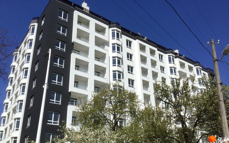 Фасад новобудови ЖК Kaiser, що складається з білих та чорних секцій, з численними балконами та вікнами. Навколо будівлі видно зелені дерева та цвітіння.