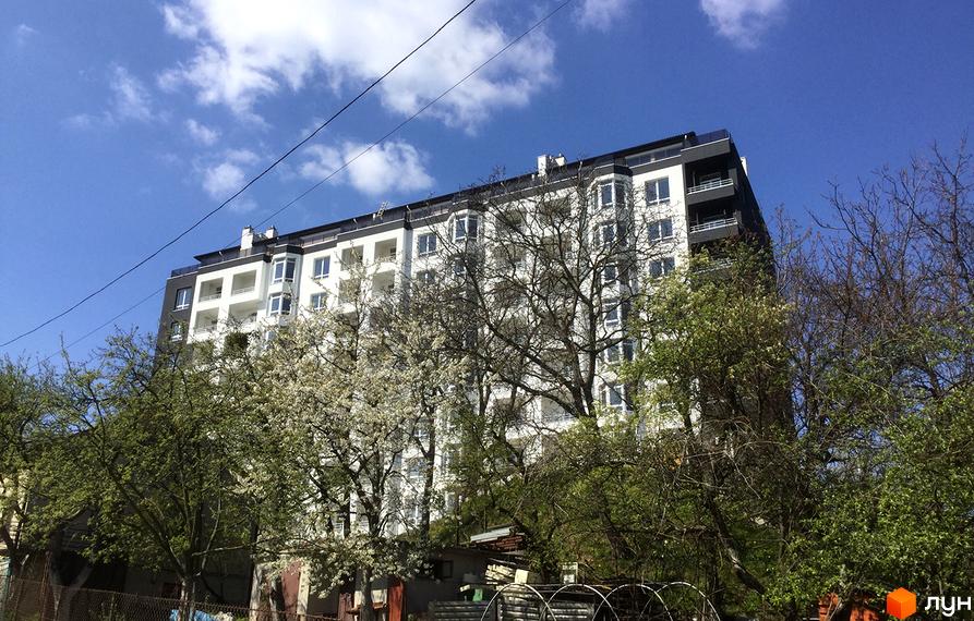 Житловий комплекс Kaiser – сучасна новобудова з біло-чорним фасадом та численними балконами. Навколо комплексу зелені дерева, деякі з них у квітах.