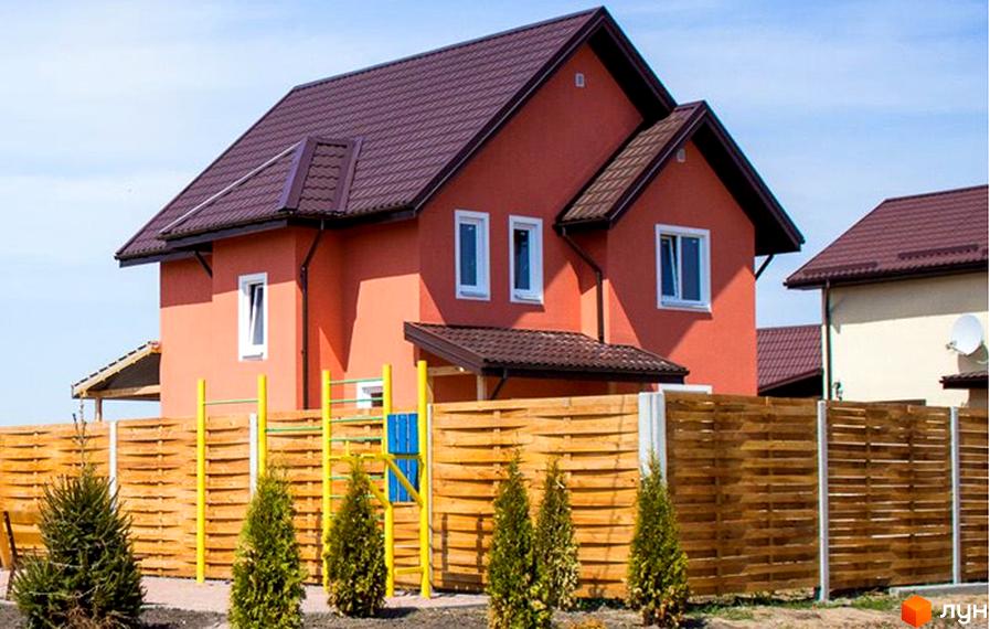 Будинок з теракотовим фасадом та коричневим дахом у Котеджному містечку Приозерний. На подвір'ї дерев'яний паркан та дитячий майданчик.