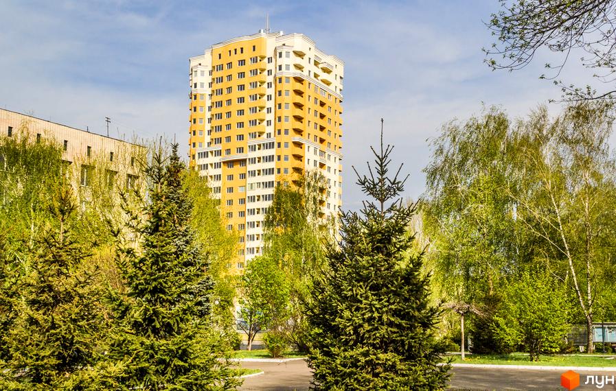 Висотна будівля ЖК Solo Park на тлі зелені дерев. Житловий комплекс має жовтий фасад з білими елементами, навколо будинку зелені насадження.