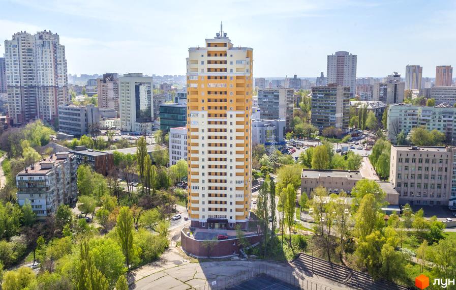 Висотна будівля ЖК Solo Park з жовто-білим фасадом. Навколо будинку зелені насадження та інші будівлі міста.