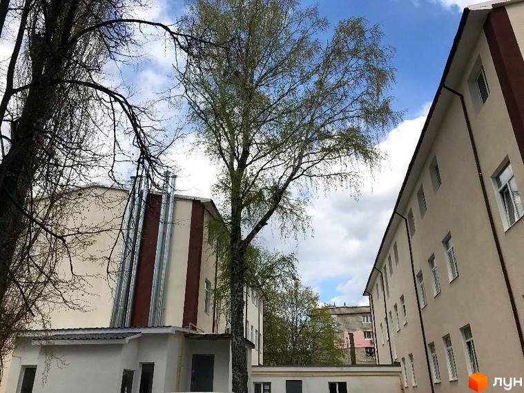 Зовнішній вигляд житлового комплексу Садове місто з фасадами світло-бежевого кольору та коричневими елементами. Навколо будівлі розташовані дерева з зеленою кроною.