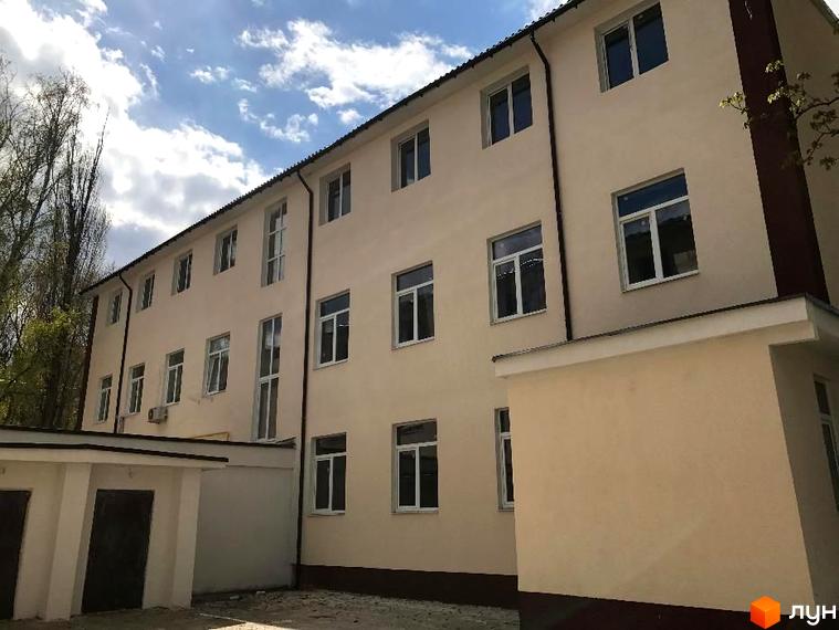 Зовнішній вигляд триповерхової новобудови ЖК Садове місто з численними вікнами. Навколо будівлі видно дерева та елементи прибудинкової території.