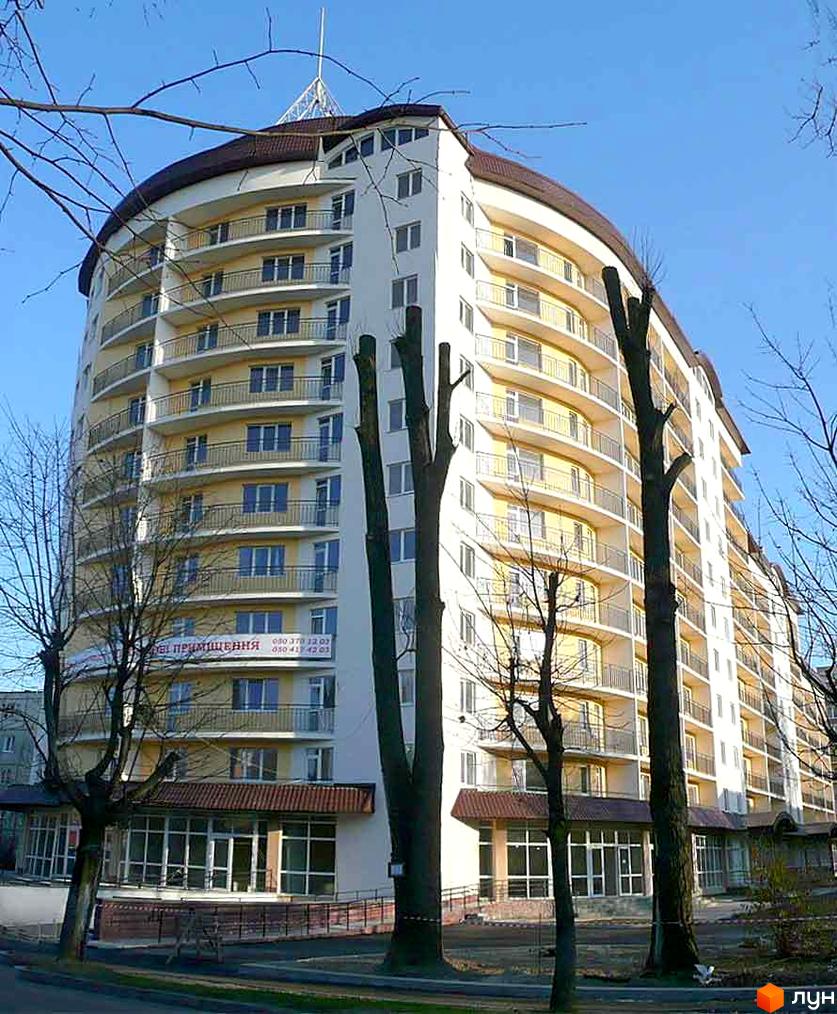 Житловий комплекс на вул. Караджича, 29: багатоповерховий будинок з вигнутим фасадом, балконами та коричневим дахом. Навколо будівлі голі дерева.