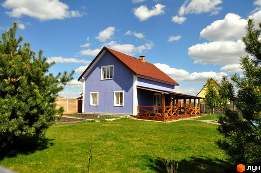 Двоповерховий будинок з синьою фасадною стіною, червоним дахом та дерев'яною терасою в Котеджному містечку HappyTown. Прибудинкова територія має зелений газон та хвойні дерева.