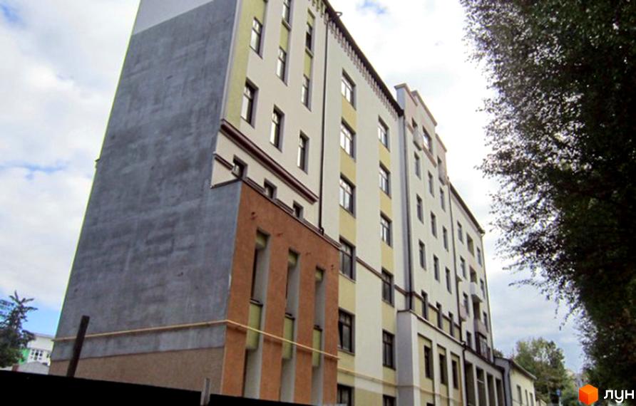 Зовнішній вигляд багатоквартирного будинку на вул. Левицького, 128. Будинок має світлий фасад з коричневими та жовтими елементами, а також сіру частину будівлі. Поруч видно дерева.