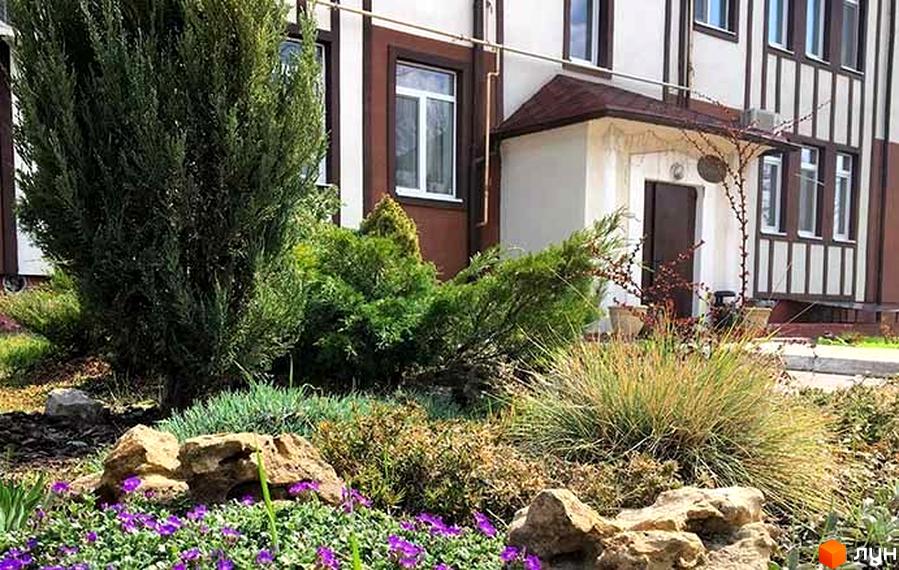 Житловий комплекс Ренесанс: фасад будинку з коричневими та білими елементами, вікна. Прибудинкова територія з зеленими насадженнями, кущами та квітами.