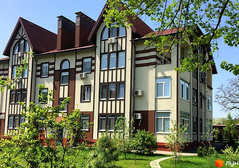 Фасад житлового комплексу Ренесанс з коричневими та бежевими елементами, вікнами та кондиціонерами. Навколо будинку зелений газон та дерева.