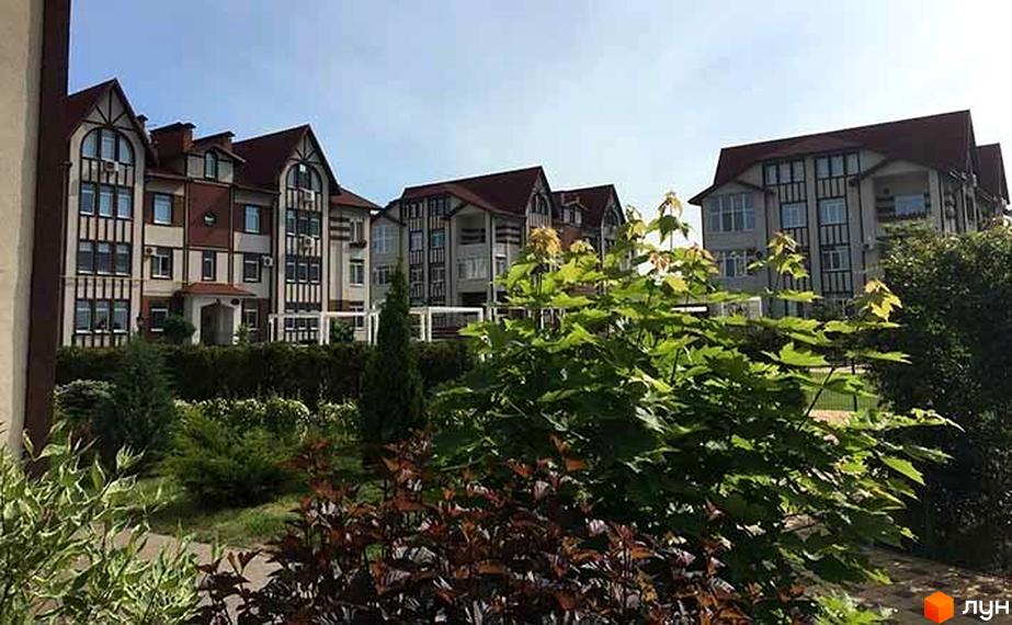 Житловий комплекс Ренесанс. Фасади будинків виконані в світлих тонах з темними дерев'яними вставками та червоним дахом. Навколо будівель зелені насадження та дерева.