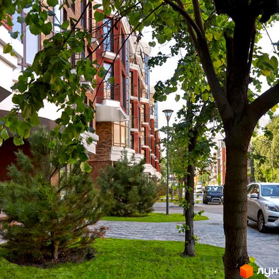 Житловий комплекс Малевича, 48, з червоної цегли з балконами та прибудинковою територією, озелененою деревами та газоном.