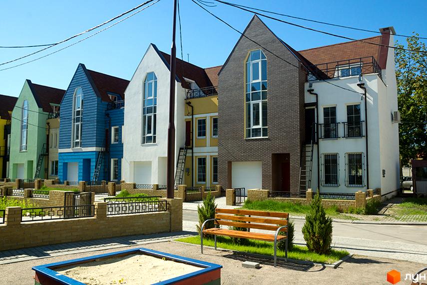 Фото таунхаусів у Житловому комплексі „Журавлевская Слобода“. Двоповерхові будинки з великими вікнами, подвір'я з лавкою та пісочницею.