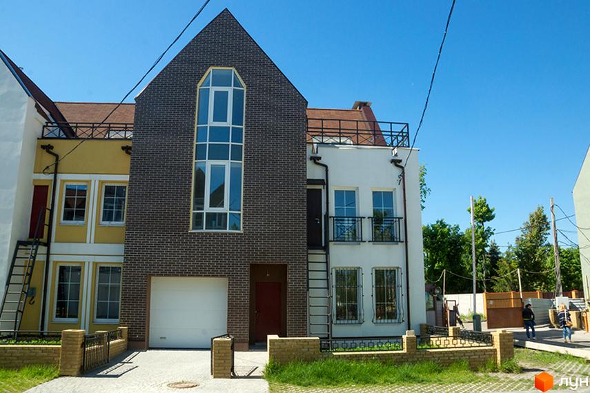 Фото Таунхаусів „Журавлевская Слобода“: триповерхові будинки з гаражами, фасади жовтого, коричневого та білого кольорів. Перед будинками газон та невисокий паркан.