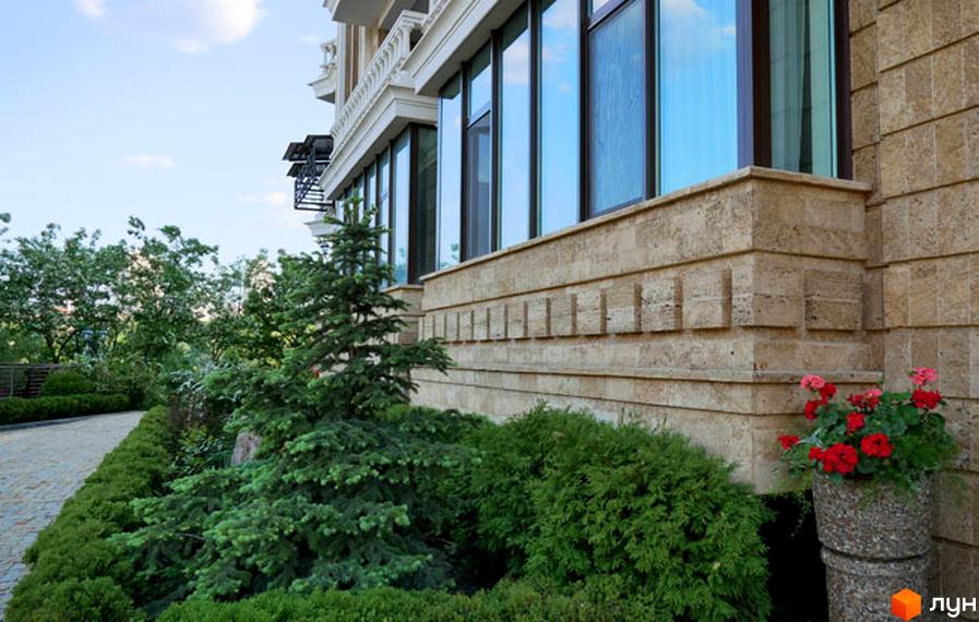 Житловий комплекс Liberty Estate з фасадом з каменю та великими вікнами. На прибудинковій території зелені насадження та квіти.