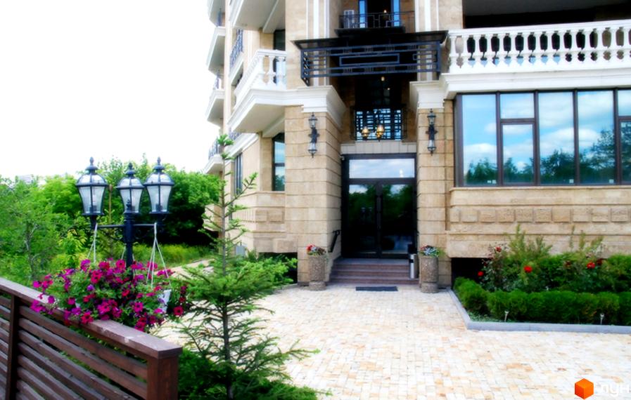 Зовнішній вигляд будинку ЖК Liberty Estate з пісковику з великими вікнами та вхідною групою. На території перед будинком викладена бруківка, є зелені насадження та ліхтарі.