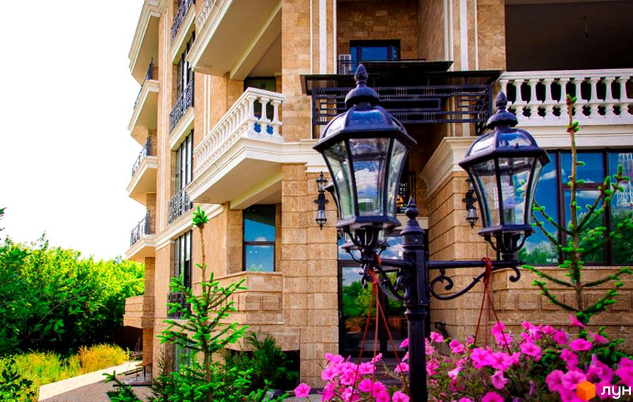 Зовнішній вигляд будинку ЖК Liberty Estate з балконами та ліхтарями. На прибудинковій території ростуть квіти та дерева.