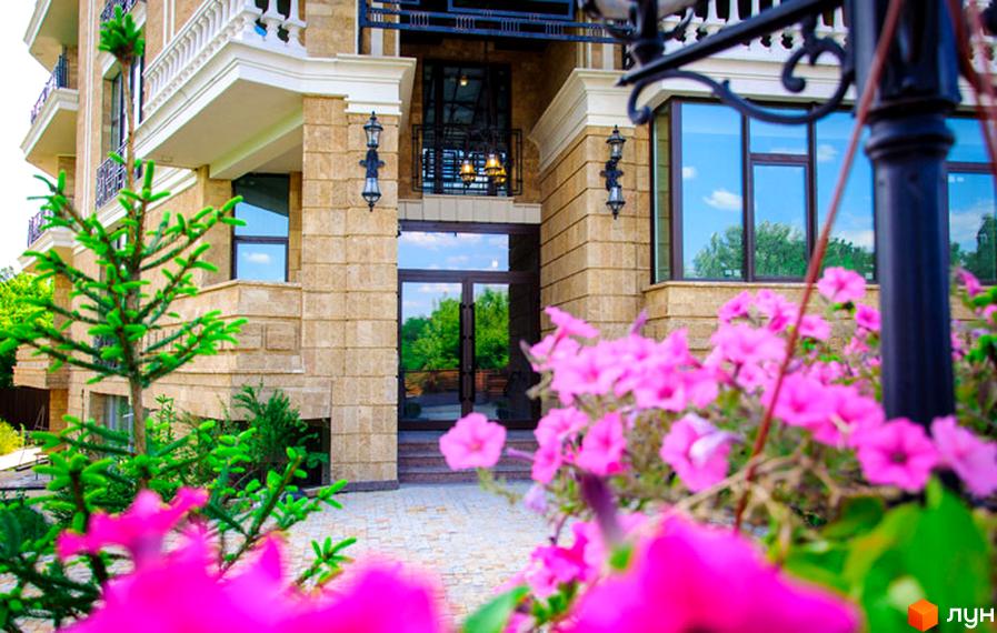 Фасад будинку ЖК Liberty Estate з великими вікнами та оздобленням з каменю. Перед будинком квіти та зелені насадження.