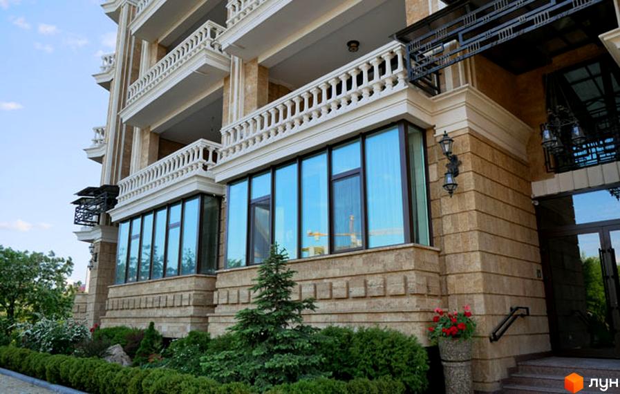 Зовнішній вигляд будинку ЖК Liberty Estate з великими вікнами та балконами. На прибудинковій території зелені насадження та декоративні рослини.