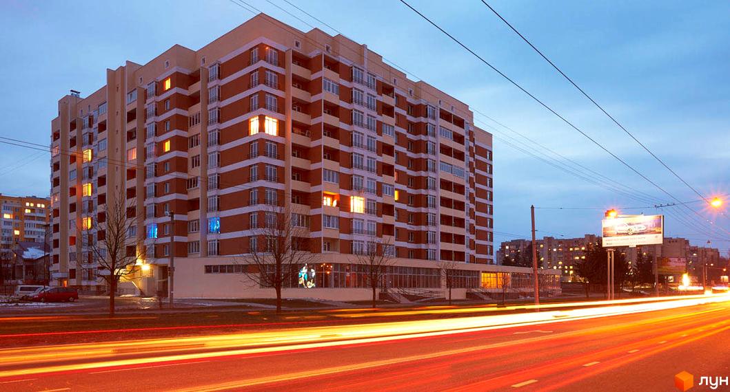 Багатоповерховий житловий комплекс на вулиці Перфецького, 2а, з цегляним фасадом та численними вікнами. Навколо будинку розташовані дерева та дорога з автомобільним рухом.