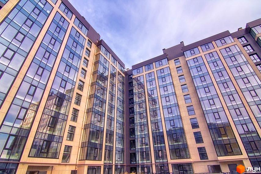 Фасад житлового комплексу Салют з великою кількістю скління та бежевими панелями. Будинок має багатоповерхову структуру та сучасний дизайн.