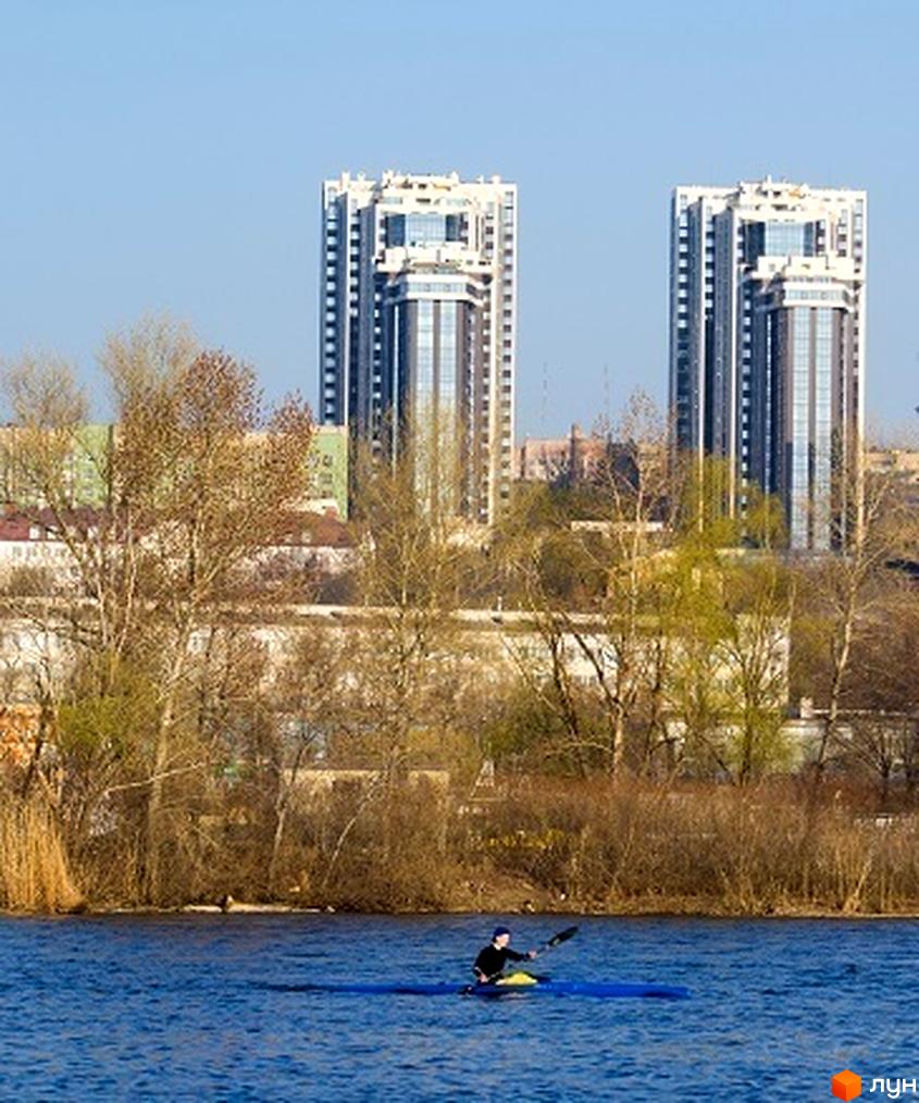 Високі будівлі ЖК Панорама на березі річки. На передньому плані вода та людина на каяку.