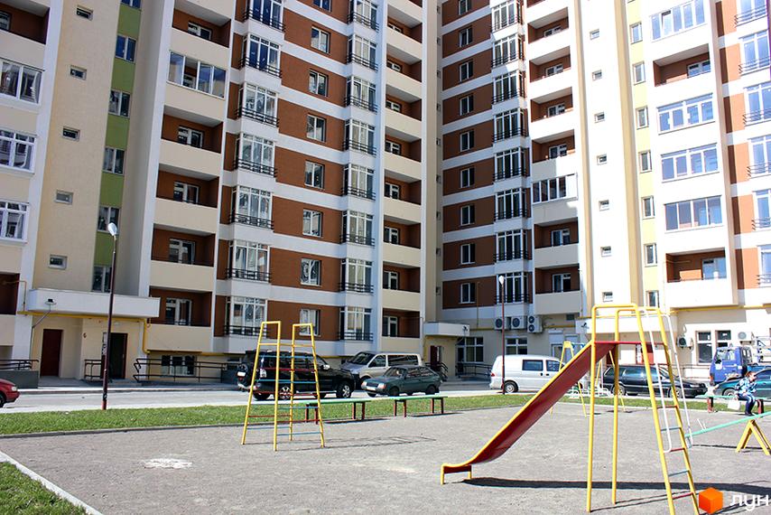 Новобудова на вул. Перфецького, 2а, з коричнево-білими фасадами та зеленими вставками. Поруч дитячий майданчик з гіркою та машинками.