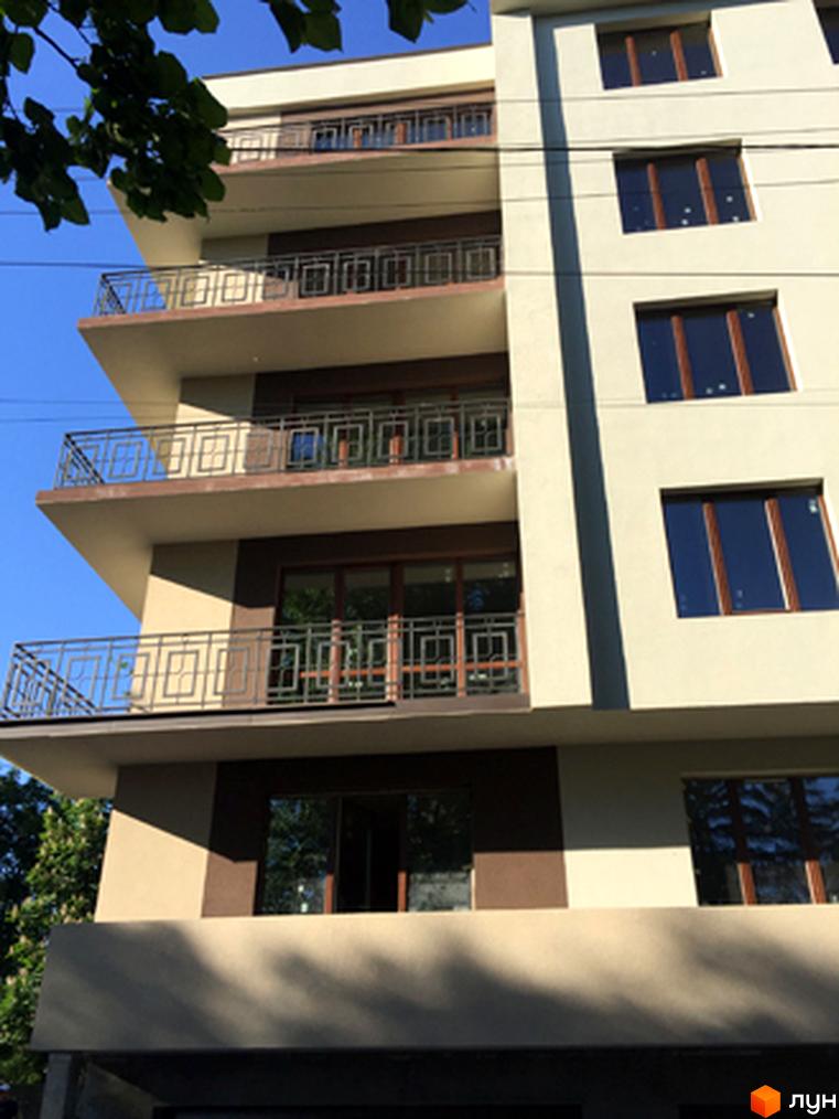 Клубний будинок Brownie House: багатоквартирний будинок зі світлим та коричневим фасадом, обладнаний балконами з металевими поручнями. Поруч ростуть дерева.