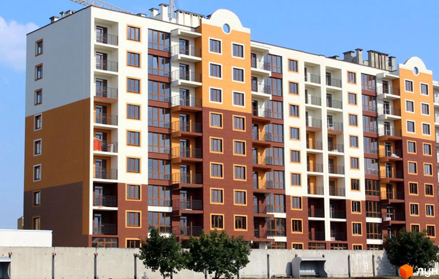 Житловий комплекс Паркове містечко - багатоповерховий будинок з коричневими та білими фасадами, балконами та великими вікнами. Територія перед будинком огороджена парканом, поруч дерева.