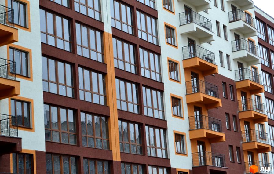 Фасад житлового комплексу Паркове містечко з коричневими та білими секціями, великими вікнами та помаранчевими балконами. Сучасна архітектура новобудови.
