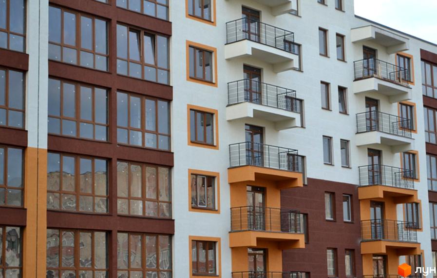 Житловий комплекс Паркове містечко – це багатоповерхова новобудова з фасадом, що поєднує білі, коричневі та помаранчеві кольори, та має багато вікон і балконів.