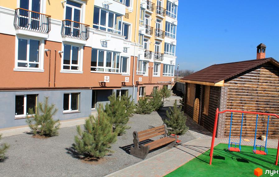 Будинок ЖК Якоря з балконами та великими вікнами. Поруч розташований дерев'яний будиночок та дитячий майданчик з гойдалками.