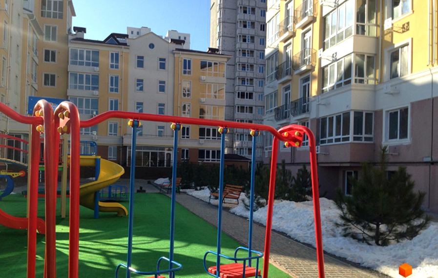 Житловий комплекс Якоря: дитячий майданчик з гіркою та гойдалками на фоні багатоповерхових будинків. Прибудинкова територія з деревами та снігом.