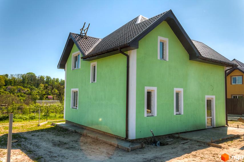 Зелений двоповерховий будинок з темним дахом та білими вікнами. Навколо будинку – будівельний майданчик з елементами благоустрою території.