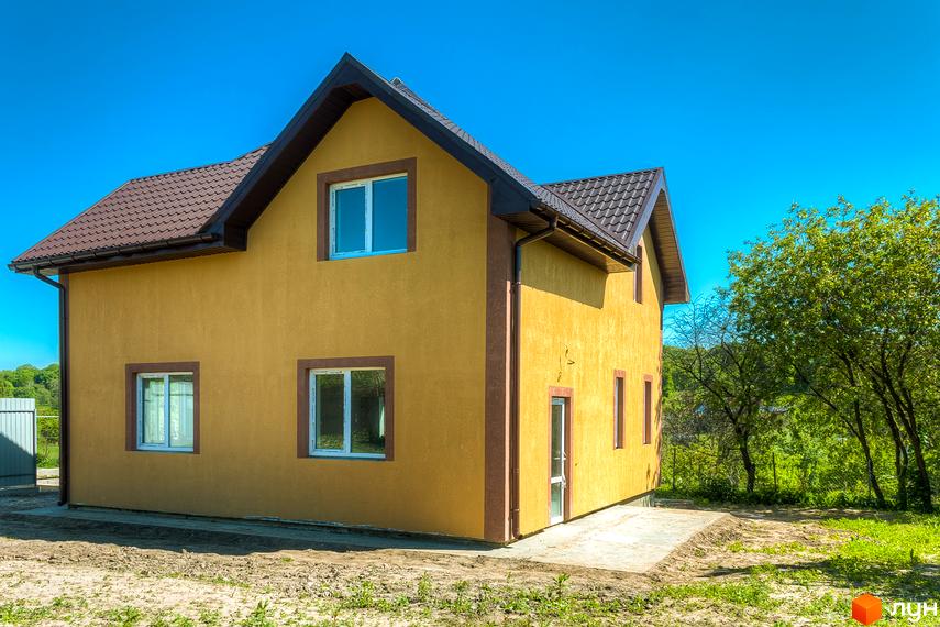 Котеджне містечко Sunhills: двоповерховий жовтий будинок з коричневим дахом та вікнами. Навколо будинку зелені дерева та галявина.