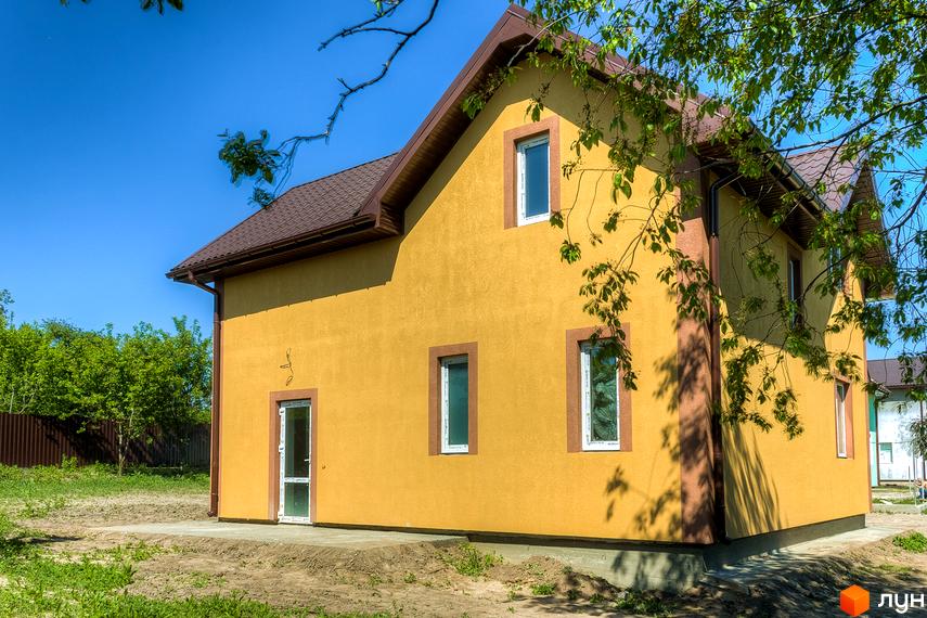 Котеджне містечко Sunhills: двоповерховий будинок жовтого кольору з коричневим дахом та вікнами під час сонячного дня. Навколо будинку зелені насадження та паркан.