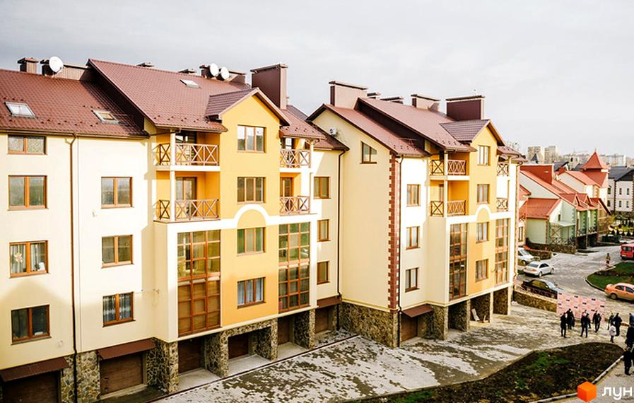 Житловий комплекс Віденська брама. Фасади будинків оздоблені світлою штукатуркою та коричневою черепицею. Прибудинкова територія з дорогою та припаркованими автомобілями.