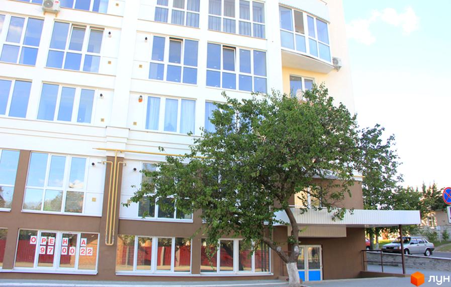 Новобудова на вулиці Милорадовичів (Петровського), 55, вул. Володимира Івасюка (Менделєєва), 5. Фасад будівлі білого кольору з коричневими елементами, багато вікон та зелене дерево перед будинком.