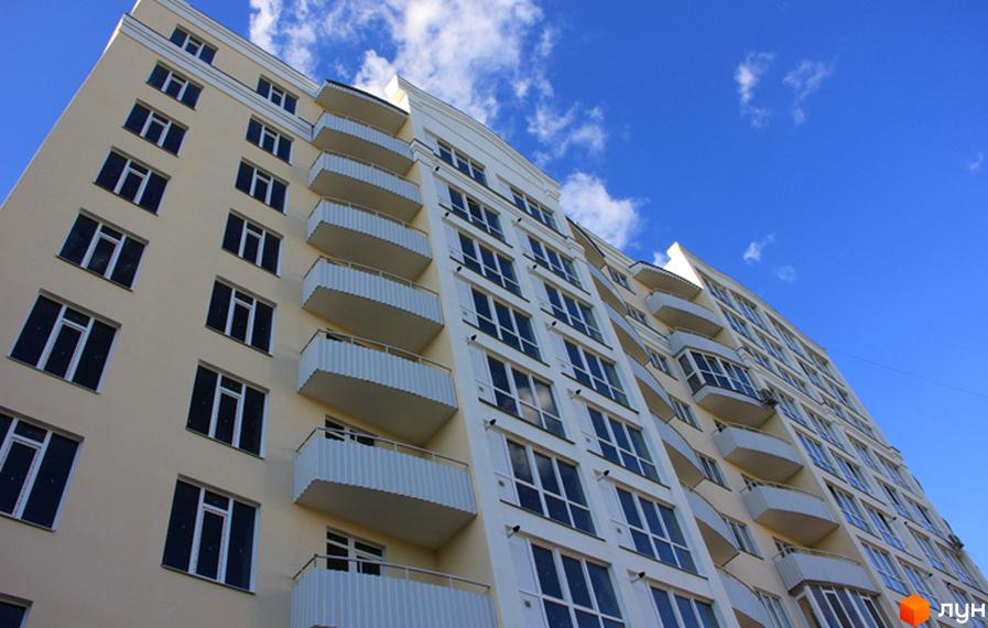 Новобудова на вулиці Милорадовичів (Петровського), 55 та Володимира Івасюка (Менделєєва), 5. Багатоповерховий будинок з балконами та великою кількістю вікон на фоні блакитного неба з хмарами.