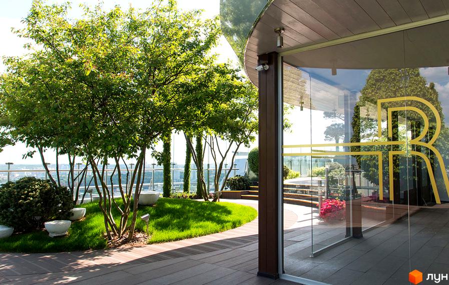 Зелена тераса з деревами та газоном біля скляного входу з логотипом ЖК Royal Tower. Відкритий простір з видом на місто.