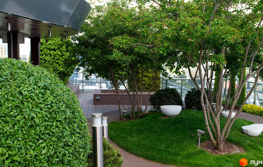 Житловий комплекс Royal Tower: частина будівлі з вигнутим дахом та облаштована тераса на даху з деревами та газоном.