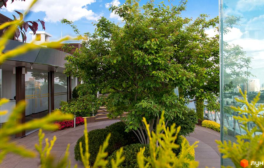 Житловий комплекс Royal Tower з багатою зеленню на терасі та міським пейзажем на фоні. Сучасний дизайн фасаду та доглянута прибудинкова територія з деревами та кущами.