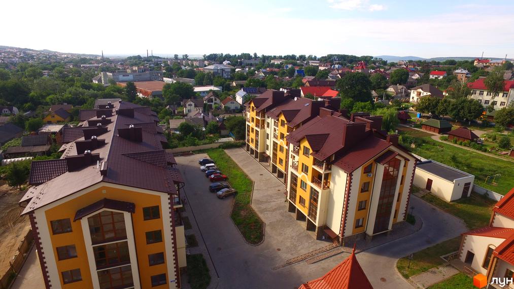 Зовнішній вигляд новобудови Віденська брама з жовтими фасадами та коричневими дахами. На прибудинковій території розташовані паркувальні місця та зелені насадження.