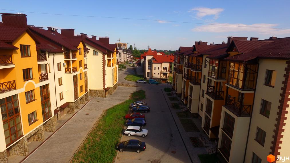 Житловий комплекс Віденська брама: фасади жовто-кремових кольорів, темні дахи, балкони. Прибудинкова територія з парковкою та зеленню.