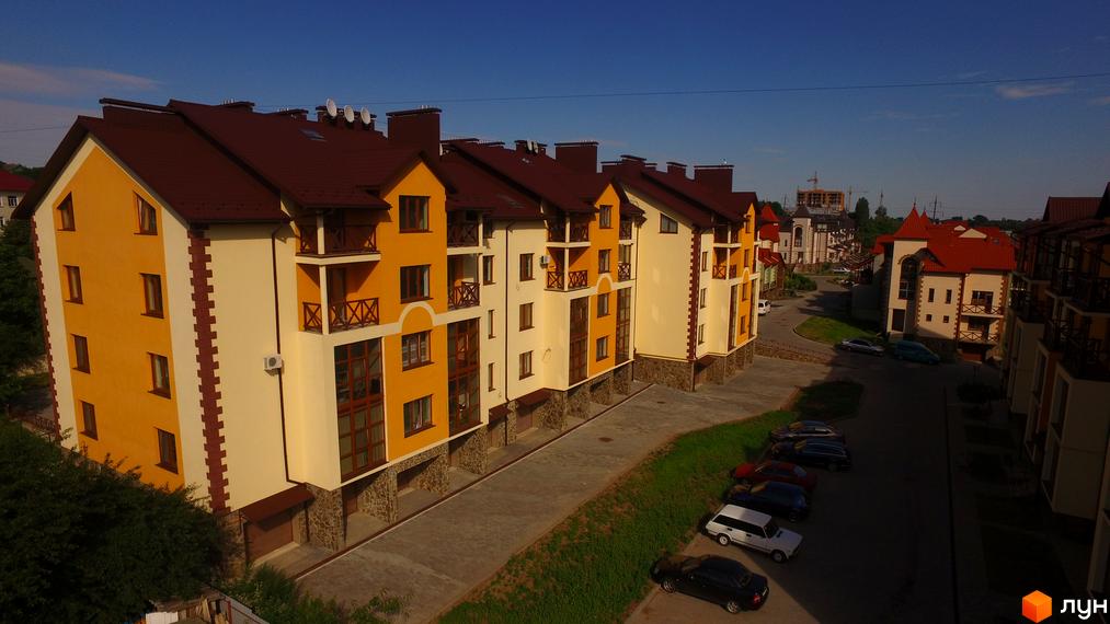 Житловий комплекс Віденська брама: фасади будинків в жовто-білих тонах з коричневими дахами, балконами та вікнами. Прибудинкова територія з доглянутими газонами та автомобілями.