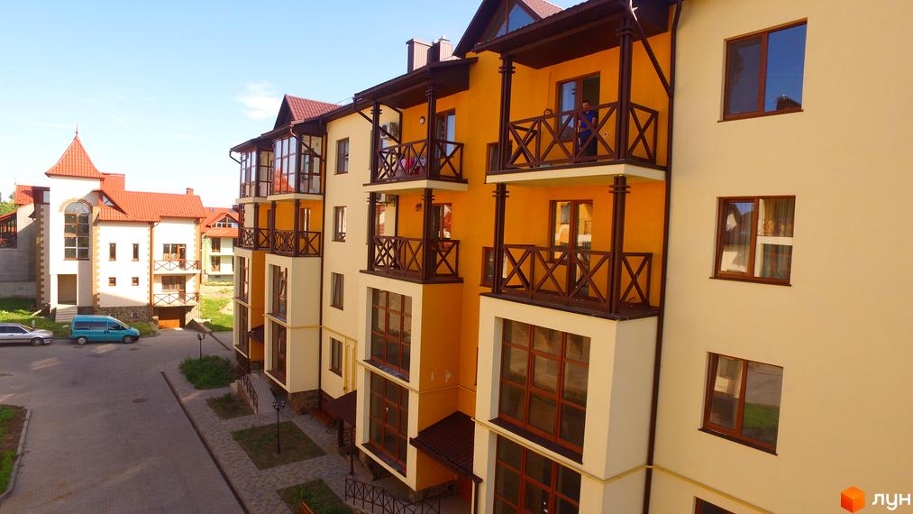 Зовнішній вигляд житлового комплексу Віденська брама з жовтими та бежевими фасадами, балконами з дерев'яними поручнями та червоними дахами. Поруч розташовані інші будинки та прибудинкова територія з дорогою та зеленими насадженнями.