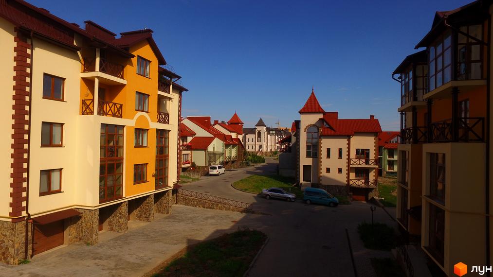 Житловий комплекс Віденська брама: фасади будинків у жовтому та бежевому кольорах з червоними дахами. Прибудинкова територія з дорогою та автомобілями.