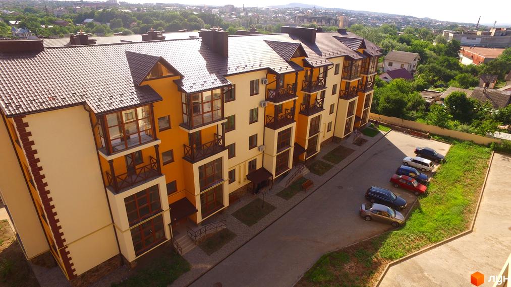 Житловий комплекс Віденська брама з жовто-бежевим фасадом та коричневим дахом. Поруч розташована парковка з автомобілями та зелена зона.