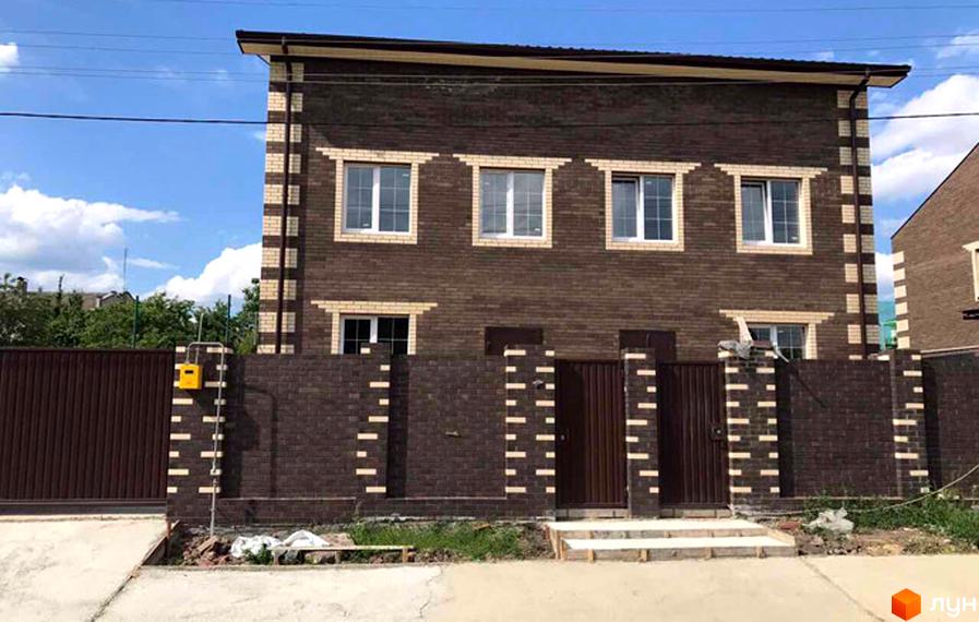 Двоповерховий будинок з коричневої цегли з білими декоративними елементами та вікнами. На прибудинковій території розташовані паркан та ворота.