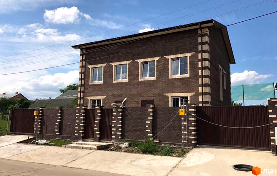 Котеджне містечко КМ Status: двоповерховий будинок з коричневої цегли з білими декоративними елементами та вікнами, огороджений цегляним парканом з коричневими воротами.